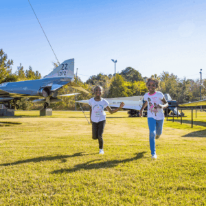 Two young girls run around Air Power Park near the air planes on display.