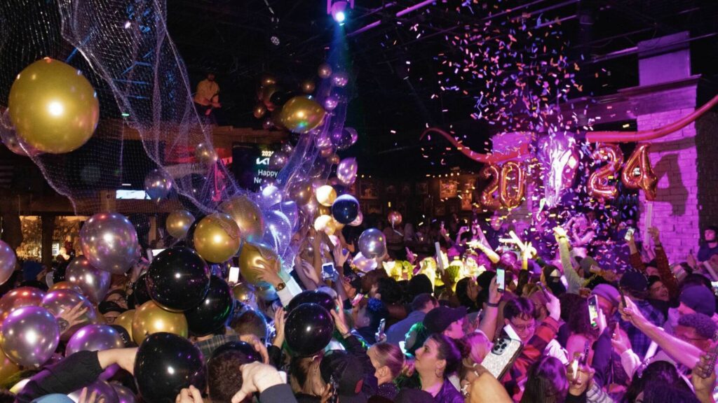 Crowd cheers amidst confetti and balloons, celebrating 2024.