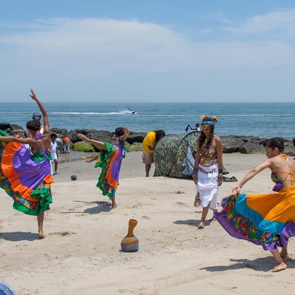 Women at beach dancing in colorful attire.