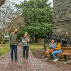 Couple exploring Fort Monroe with trail guides. Nearby women chat on bench next to historic canon.