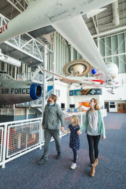 Family holding hands look up at airplanes hanging inside the Virginia Air & Space Science Center