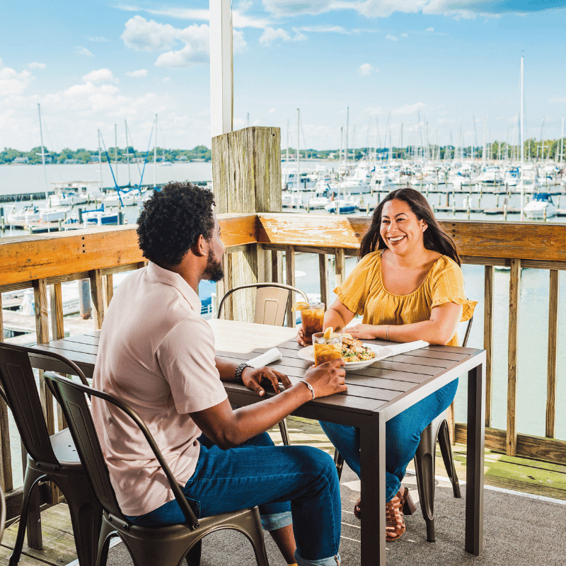 Couple eating pasta dish at Deadrise restaurant with boats in harbor in background.